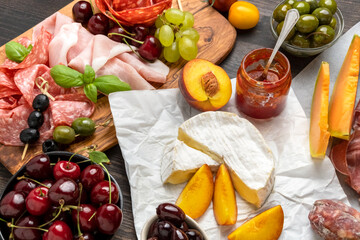 Festive Food for a christmas or thanksgiving or birthday party salami, parma ham, prosciutto with melon, pecorino and parmesan cheeses board, camembert cheese with red sauce and peaches grapes cherrie