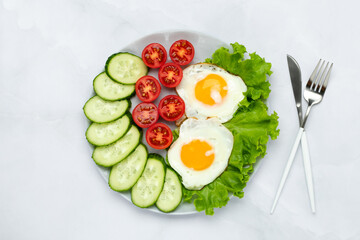 Fried chicken eggs with vegetables on a gray table. Breakfast concept. Top view. Food background in morning. Fresh sliced cucumbers and tomatoes. Flat lay composition. Overhead view.