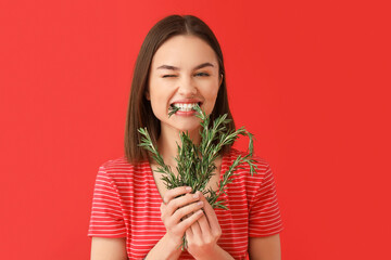 Young woman eating rosemary on color background