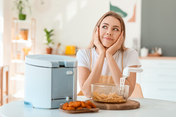 Young woman with deep fryer and snacks in kitchen