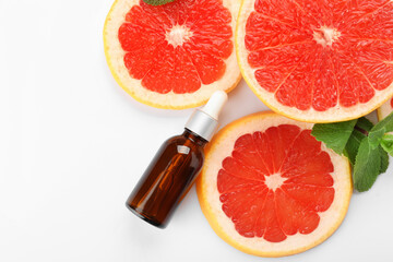 Bottle of essential oil and slices of grapefruit on white background
