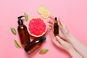Female hands with bottles of essential oil and citrus fruits on color background