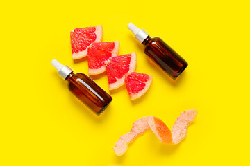 Bottles of essential oil and grapefruit slices on color background