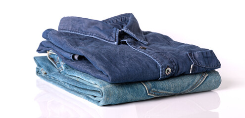 close up, stack of folded clothing jeans. pile of different color shirts, sweaters and other garments isolated on white background with copy space.