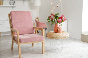 Armchair and protea flowers on pouf in interior of room