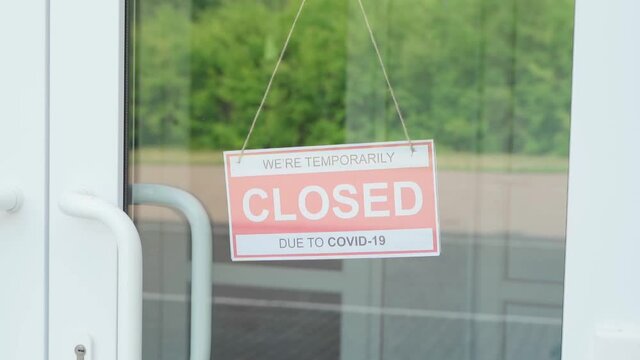 A man removes a sign that read CLOSED during the COVID-19 pandemic that hung on a transparent door or in a storefront. Slow motion