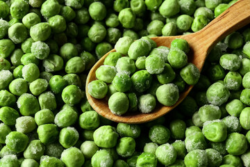 Spoon with frozen green peas as background