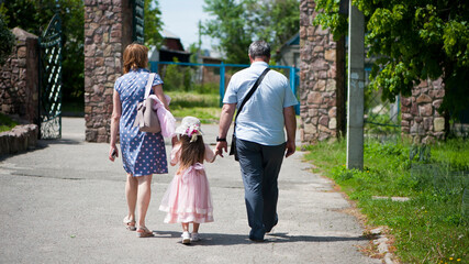 Obraz premium family walking in the park. mom dad and little girl walking holding hands. back view. daughter in a pink dress. friendly loving family concept, love. outdoor, walk in the fresh air, threesome