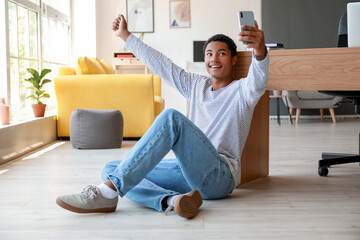 Happy African-American teenage boy taking selfie at home