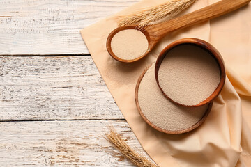 Bowls and spoon with active dry yeast on light wooden background