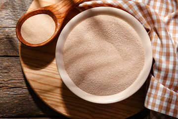 Composition with bowl of active dry yeast on wooden background