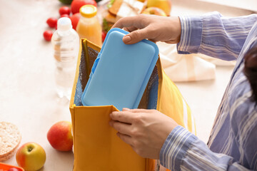 Woman packing meal into lunch box bag on light background, closeup
