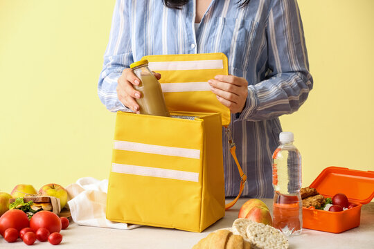 Woman packing bottle of juice into lunch box bag on color background