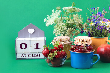 Fototapeta na wymiar Calendar for August 1 : the name of the month of August in English, cubes with the numbers 0 and 1, bouquets of wild flowers, jars of jam, strawberries and cherries in cups, green background