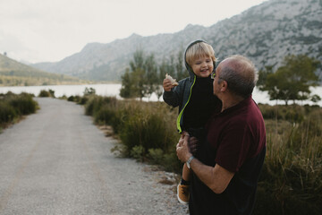 Little caucasian blond kid having fun and smiling outdoors with his grandfather at the mountains
