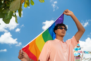 Portrait of young Hispanic gay boy looking at camera, holding LGBT flag - Focus on face landscape imagin