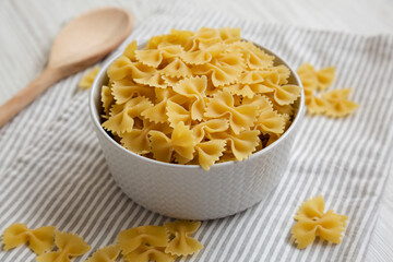 Dry Organic Farfalle Pasta in a Bowl on a white wooden background, side view.