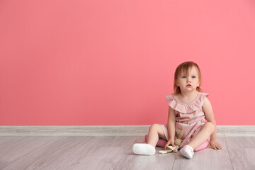 Cute baby girl sitting near color wall
