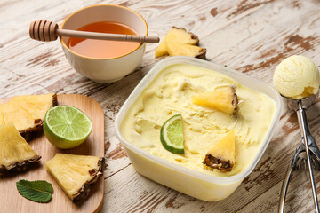 Container with tasty pineapple ice cream on light wooden background