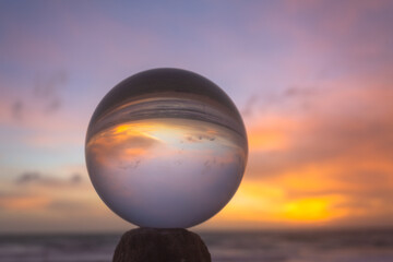 .view on the beach in beautiful sunset inside crystal ball placed on a timber by the sea. .Unconventional and beautiful natural views on the beach and sunset in a magic crystal ball. .