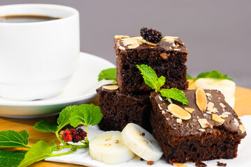 chocolate brownie cake dessert with berry and bananas slices on  wooden table. blur coffee cup in background