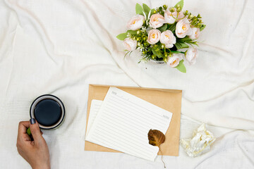 flat lay wedding card envelope and coffee cup with  and bouquet of flower's in bed, hand drink a coffee