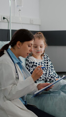 Obraz premium Mother discussing with sick little daughter while african american nurse arrange bed during medical examination in hospital ward. Physician doctor explaining sickness treatment monitoring symptoms