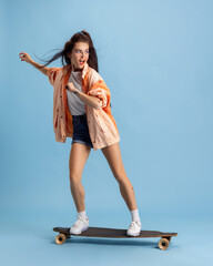 Beautiful adorable young girl in retro 90s fashion style, outfits on skateboard isolated over pink studio background. Concept of eras comparison, beauty, fashion and youth.