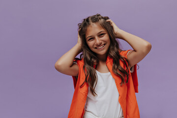 Smiling curly young girl ruffles hair in purple background. Attractive teenager in orange sweater...