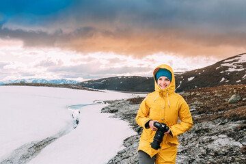 Aurlandsfjellet, Norway. Happy Young Woman Tourist Traveler Photographer With Camera Walking Near Aurlandsfjellet Scenic Route Road. Active Lifestyle In Norwegian Nature