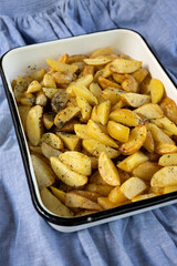 Closeup of fresh fried potato wedges in the white baking tray, blue tablecloth
