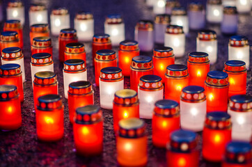 Lots of burning candles arranged in rows on the pavement.