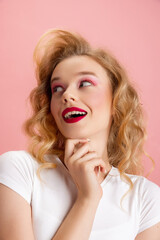 Close-up adorable pretty young girl with bright makeup and hairdo in retro 90s fashion style isolated over pink studio background. Concept of eras comparison, beauty, fashion and youth.