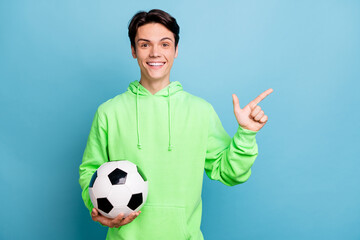 Photo of pretty charming gentleman wear green sweatshirt smiling holding ball pointing empty space...