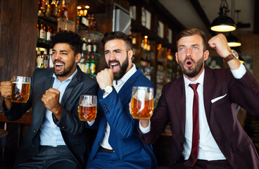 Men fans screaming and watching football on TV and drink beer in a pub