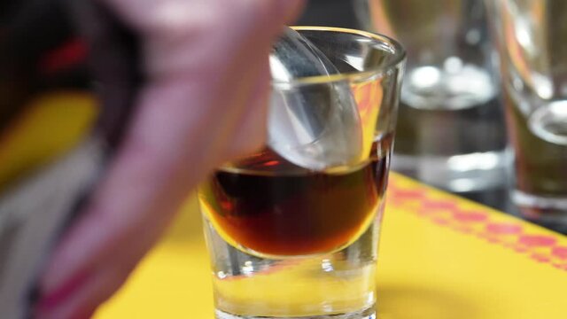 Pouring Irish Cream Through The Back Of A Cold Spoon Into A Shot Glass With Coffee Liqueur. B-52 Cocktail Layering Technique. closeup