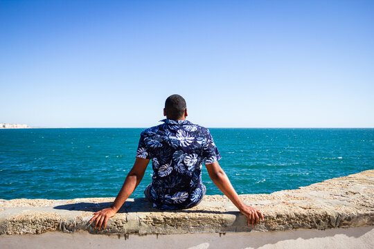 A black man facing the sea along the coast of the city