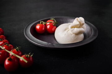 Italian burrata cheese and branch of cherry tomatoes on dark plate. Selective focus. close up. Low key