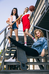 Three young girls in retro 90s fashion style, outfits posing on stairs, outdoors. Concept of eras...