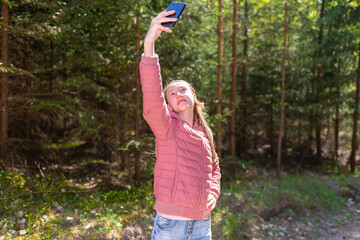 Young teen girl traveler taking selfie on mobile phone in a summer day forest. girl looking at smartphone camera.