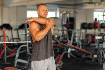 Fototapeta na wymiar Fitness man warming up in gym. Male doing warm up stretching workout on gym background.
