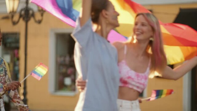 A group of multiethnic happy people are walking on the street holding and waving lgbt colorful flag