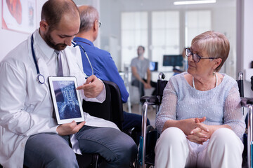 Specialist doctor showing x ray to elderly woman in wheelchair communicating test result using...