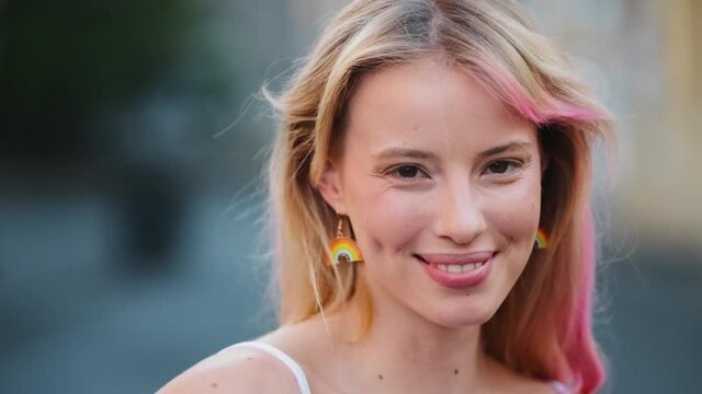 A smiling woman with colorful lgbt earrings is waving colorful flag during pride gay parade