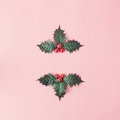 Creative layout made of winter plants and red berries on a pastel pink background with copy space. Minimal christmas composition. Flat lay.