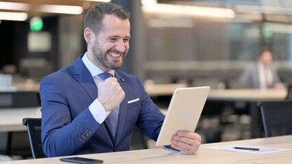 Successful Middle Aged Businessman Celebrating on Tablet at Work