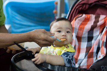 Cute Asian boy wearing a blue shirt. sitting on a black stroller and eating