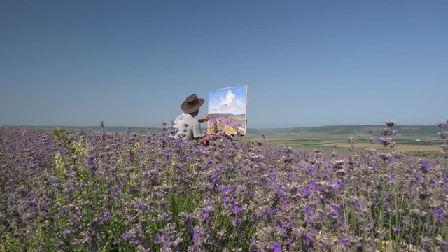 Plein air outdoors oil painting. Rural landscape, blooming lavender fields. A male artist draws a picture on canvas using an easel
