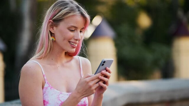 A pleased woman with rainbow earrings is using her phone during pride gay parade