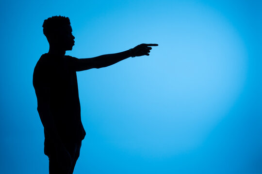 Silhouette of black man pointing aside in studio